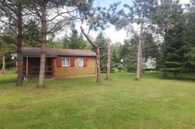 Des personnes assises en extérieur assistent à une cérémonie devant des tables décorées, près de chalets en bois.