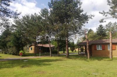 Des personnes assises en extérieur assistent à une cérémonie devant des tables décorées, près de chalets en bois.