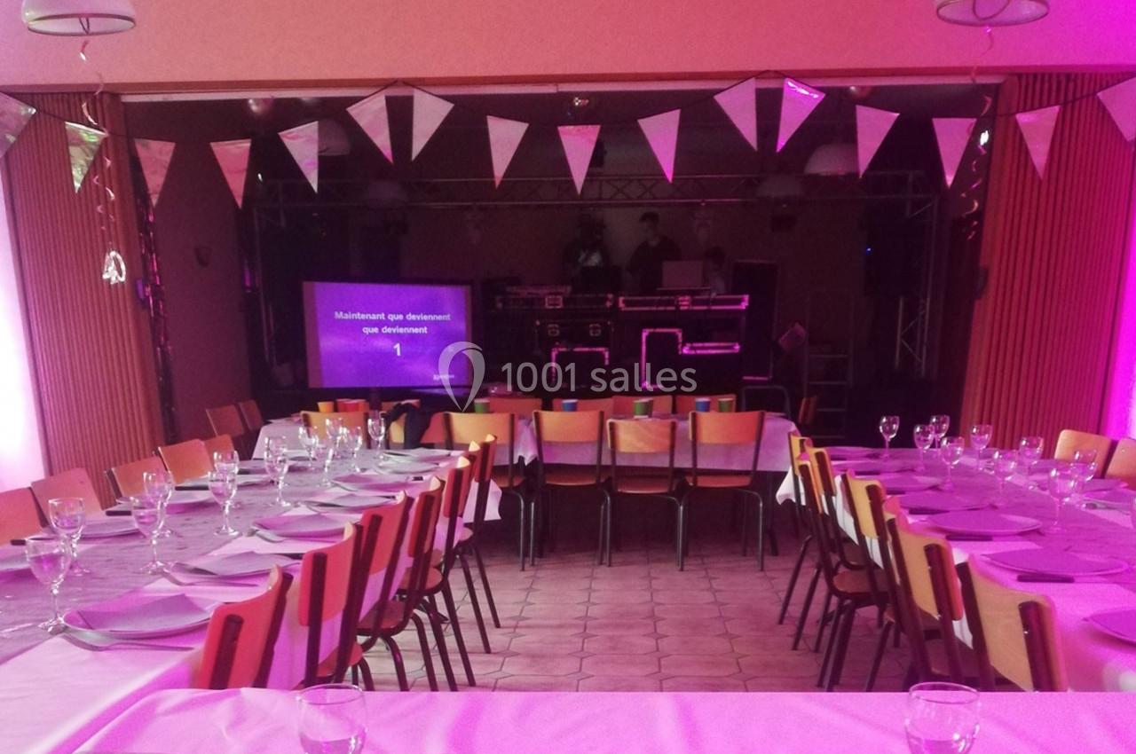 Salle décorée pour un événement avec tables dressées, guirlandes de fanions et équipement de sonorisation en fond.