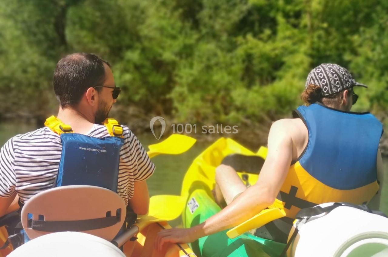 Deux personnes pagayant dans des kayaks jaunes sur une rivière entourée de végétation verdoyante.