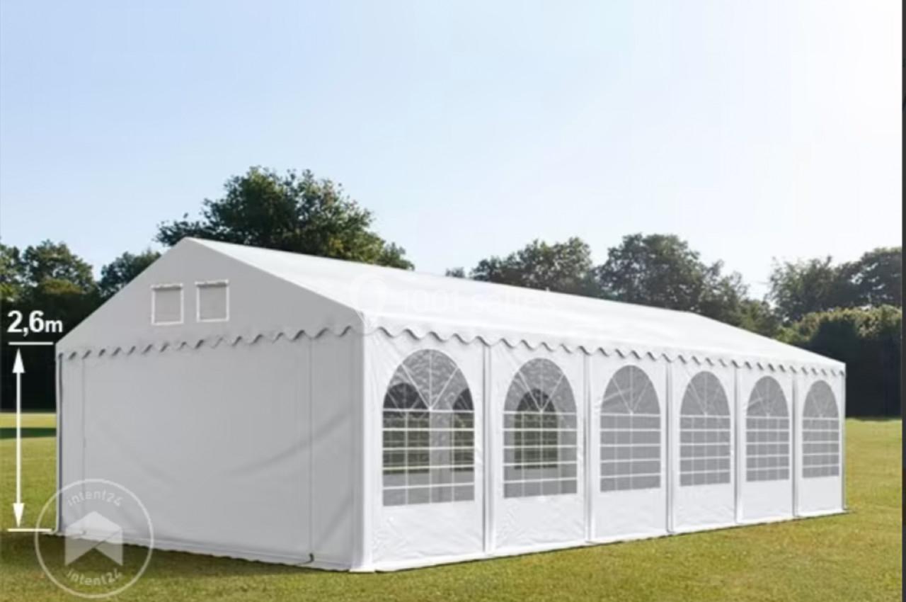Tente blanche rectangulaire avec fenêtres en arc, installée sur une pelouse, entourée d'arbres.
