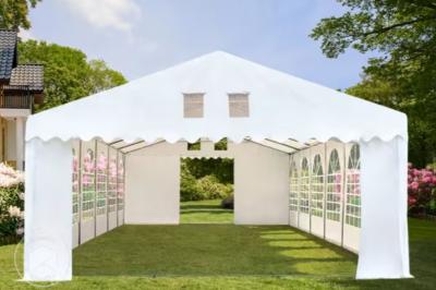 Des personnes assises en extérieur assistent à une cérémonie devant des tables décorées, près de chalets en bois.