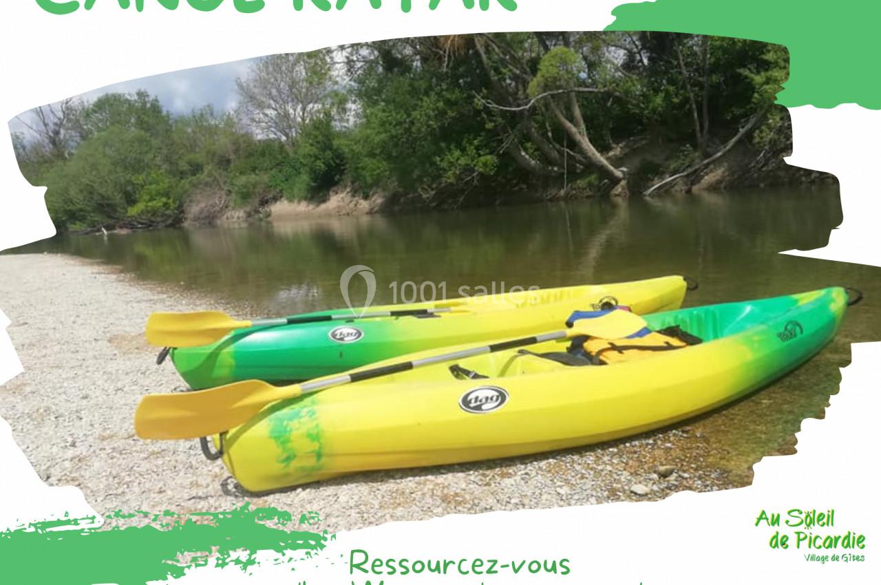 Trois canoës-kayaks jaunes et verts alignés sur une rive sablonneuse près d'une rivière bordée d'arbres.