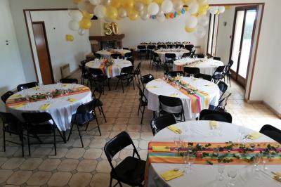 Des personnes assises en extérieur assistent à une cérémonie devant des tables décorées, près de chalets en bois.