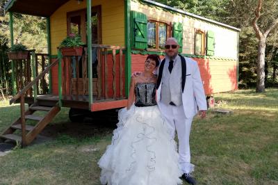 Des personnes assises en extérieur assistent à une cérémonie devant des tables décorées, près de chalets en bois.