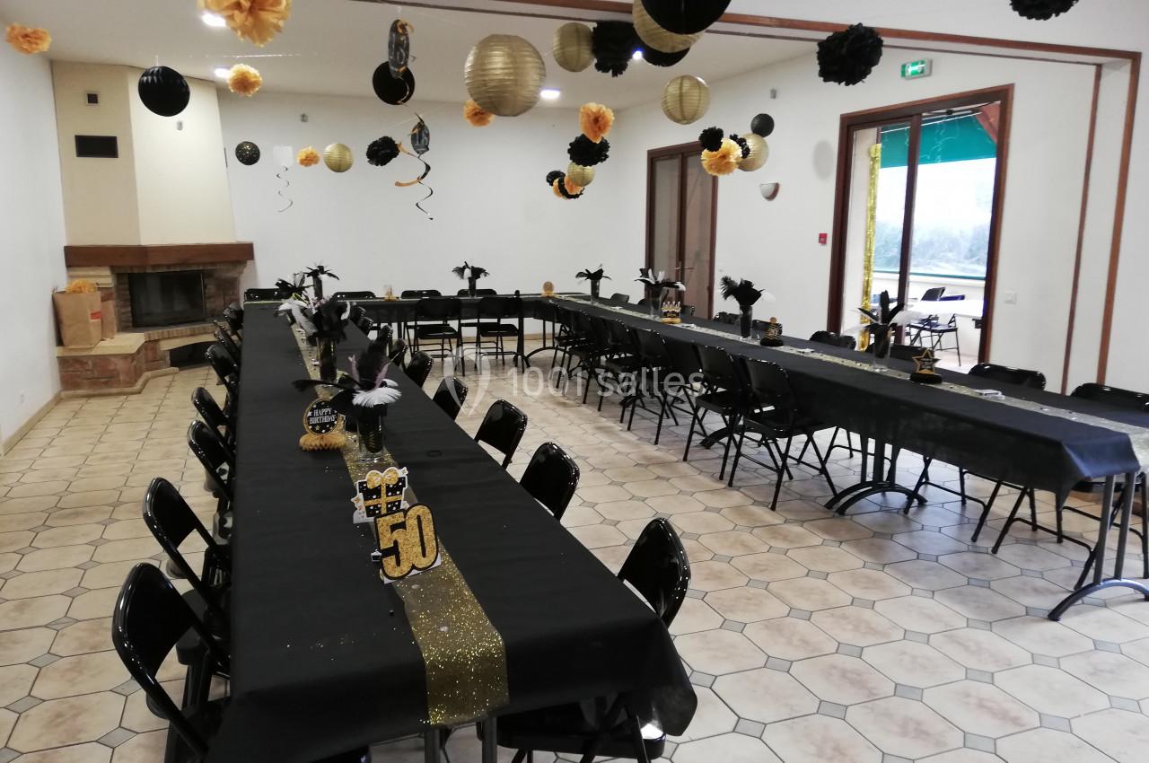 Salle décorée en noir et or avec des tables alignées pour une fête, ornées de ballons et d'éléments festifs.