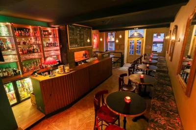 Intérieur d'un bar chaleureux avec tables rondes, bougies, grand miroir, comptoir en bois et menu affiché au mur.