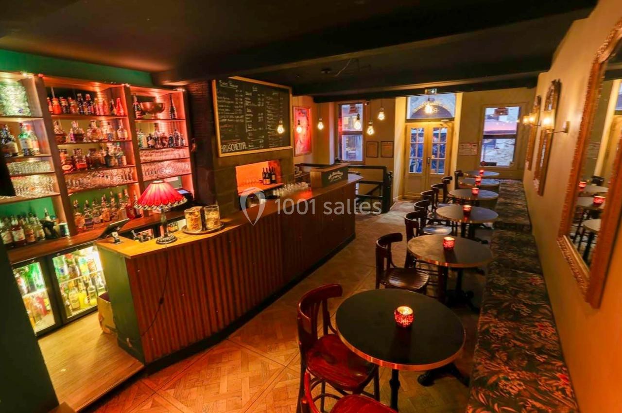 Intérieur d'un bar chaleureux avec comptoir en bois, étagères de bouteilles et petites tables éclairées par des bougies.