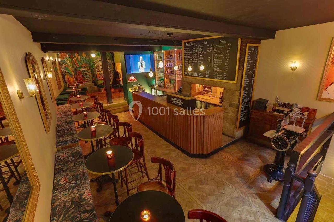 Intérieur d'un bar chaleureux avec comptoir en bois, tables éclairées par des bougies et décorations murales colorées.
