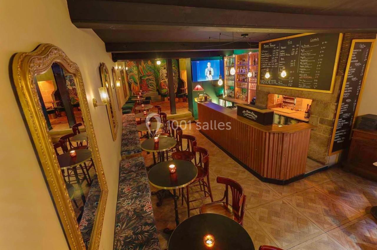 Intérieur d'un bar chaleureux avec tables rondes, bougies, grand miroir, comptoir en bois et menu affiché au mur.