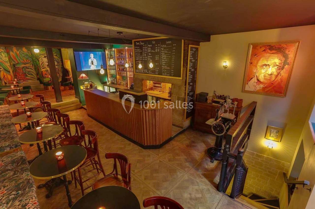Intérieur d'un bar chaleureux avec comptoir en bois, tables rondes, éclairage tamisé et décorations artistiques.