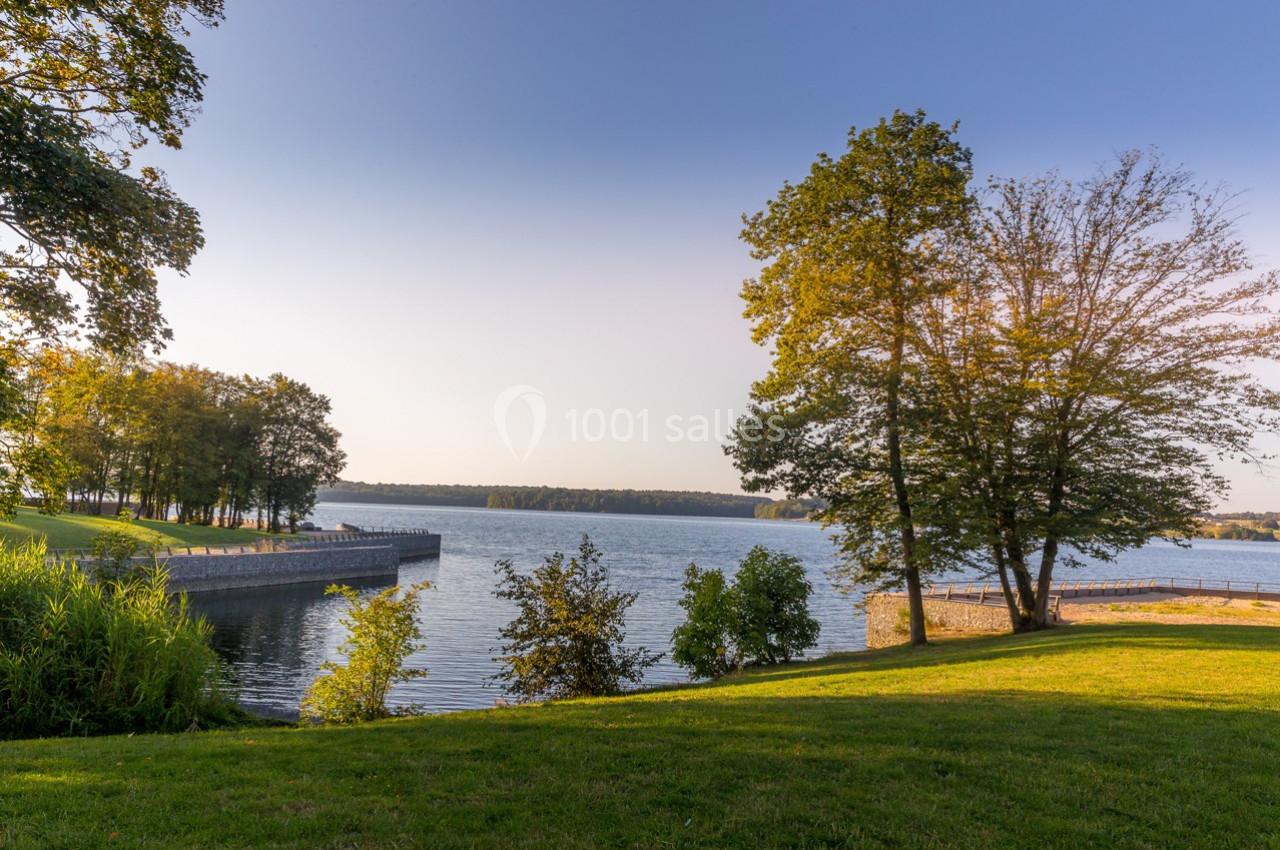 Vue d'un lac entouré d'arbres et de pelouses verdoyantes sous un ciel dégagé en fin de journée.