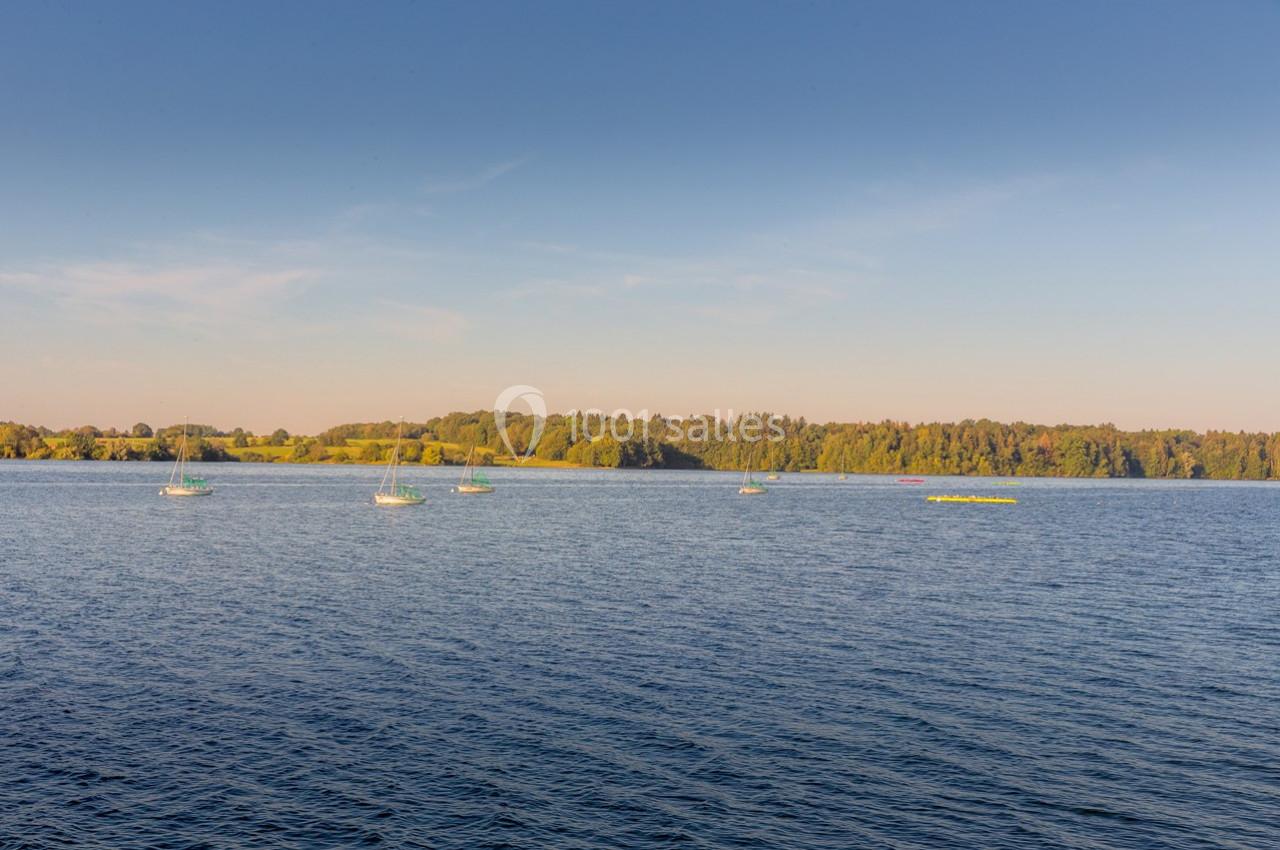 Vue d'un lac calme avec des voiliers dispersés et une forêt en arrière-plan sous un ciel dégagé.
