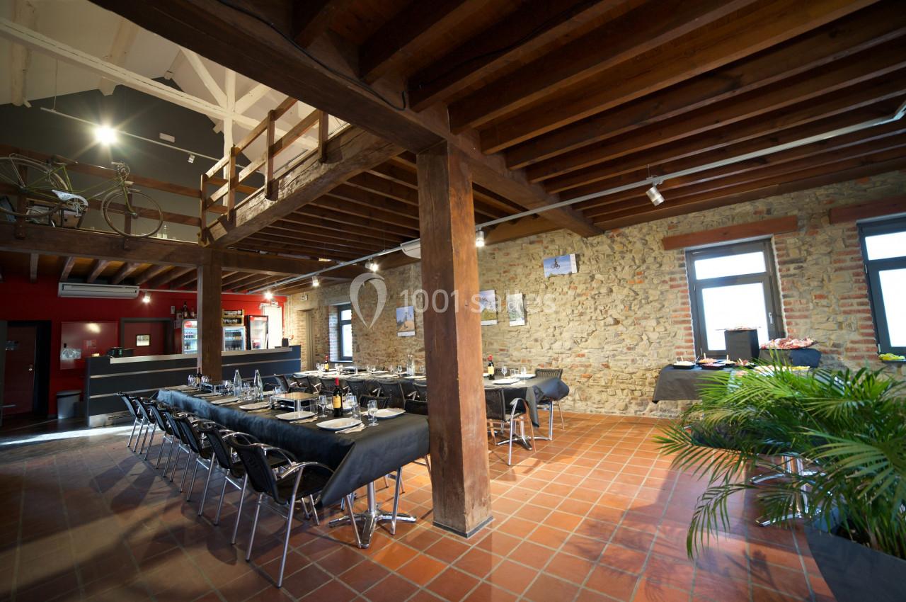 Salle de réception avec tables dressées, murs en pierre, poutres apparentes et lumière naturelle.