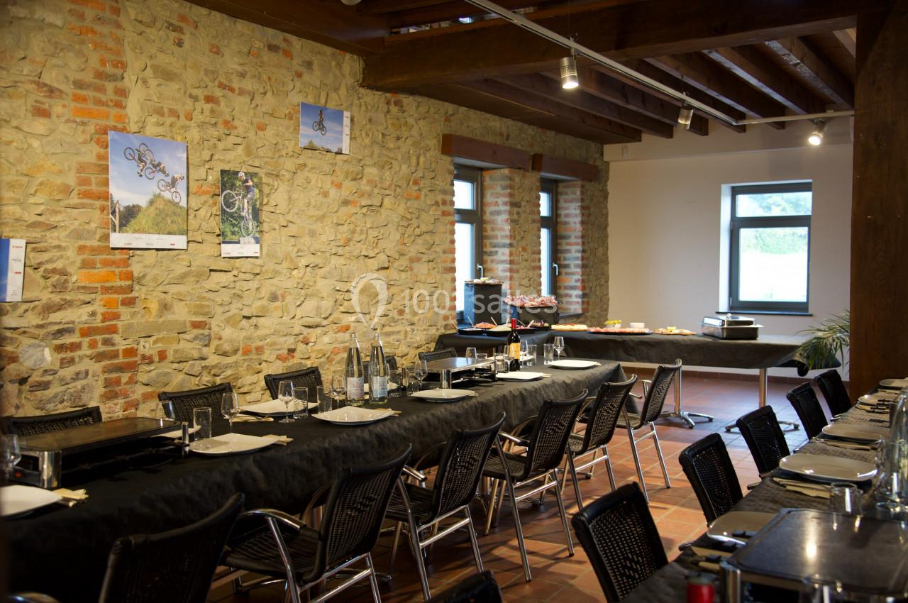 Salle à manger avec murs en pierre, tables dressées pour un repas et buffet installé près des fenêtres.