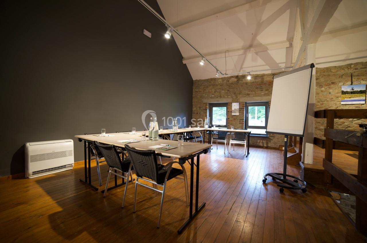 Salle de réunion lumineuse avec tables, chaises, paperboard et bouteilles d'eau sur un sol en bois.