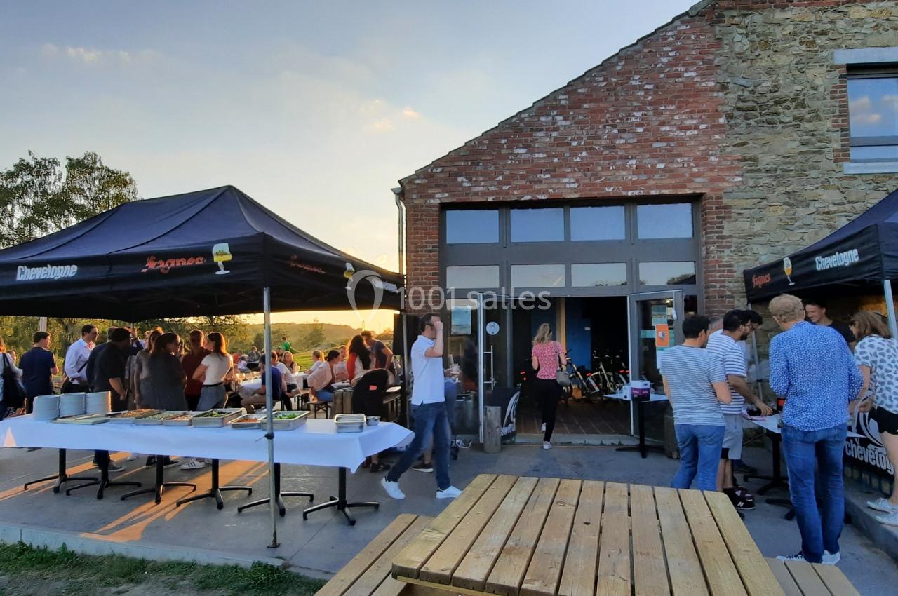 Groupe de personnes réunies en extérieur près d'un bâtiment en pierre, avec des stands sous des tentes noires.