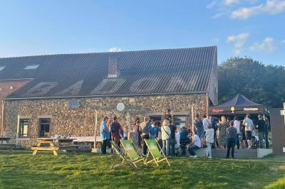 Groupe de personnes rassemblées devant une maison en pierre avec un chapiteau, sur une pelouse par temps ensoleillé.