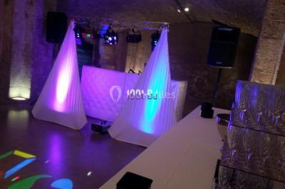 Salle de réception avec éclairage coloré, piste de danse vide et deux personnes debout près d'un bar lumineux.