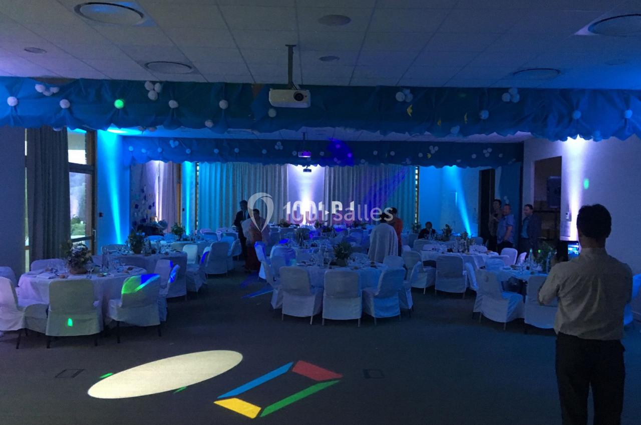 Salle de réception décorée avec des tables rondes, nappes blanches et éclairage tamisé bleu.
