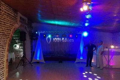 Salle de réception avec éclairage coloré, piste de danse vide et deux personnes debout près d'un bar lumineux.