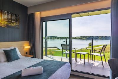 Terrasse en bois avec table et chaises, vue sur un jardin verdoyant et un lac au coucher du soleil.