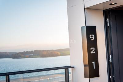 Terrasse en bois avec table et chaises, vue sur un jardin verdoyant et un lac au coucher du soleil.