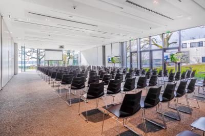 Terrasse en bois avec table et chaises, vue sur un jardin verdoyant et un lac au coucher du soleil.