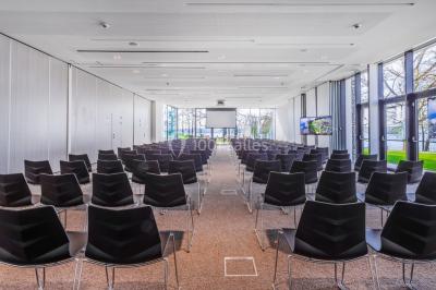 Terrasse en bois avec table et chaises, vue sur un jardin verdoyant et un lac au coucher du soleil.