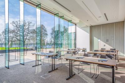Terrasse en bois avec table et chaises, vue sur un jardin verdoyant et un lac au coucher du soleil.