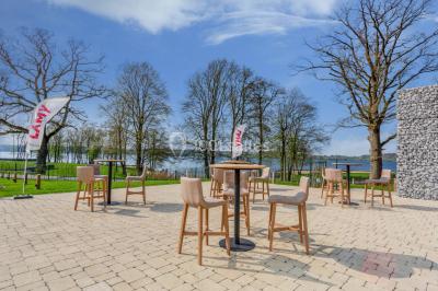Terrasse en bois avec table et chaises, vue sur un jardin verdoyant et un lac au coucher du soleil.
