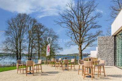 Terrasse en bois avec table et chaises, vue sur un jardin verdoyant et un lac au coucher du soleil.