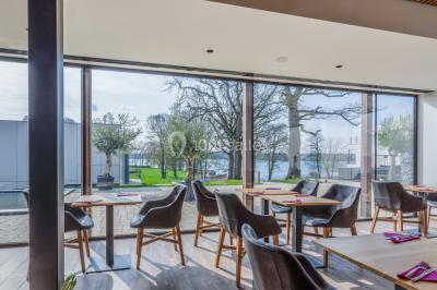 Terrasse en bois avec table et chaises, vue sur un jardin verdoyant et un lac au coucher du soleil.