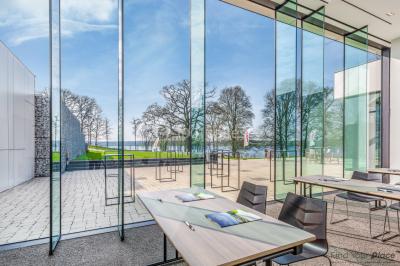 Terrasse en bois avec table et chaises, vue sur un jardin verdoyant et un lac au coucher du soleil.