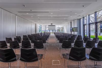 Terrasse en bois avec table et chaises, vue sur un jardin verdoyant et un lac au coucher du soleil.