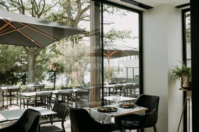 Terrasse en bois avec table et chaises, vue sur un jardin verdoyant et un lac au coucher du soleil.