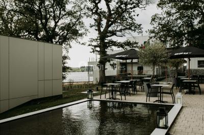 Terrasse en bois avec table et chaises, vue sur un jardin verdoyant et un lac au coucher du soleil.