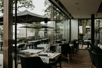 Terrasse en bois avec table et chaises, vue sur un jardin verdoyant et un lac au coucher du soleil.