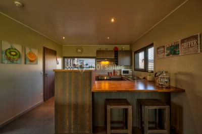 Terrasse en bois avec table et chaises, vue sur un jardin verdoyant et un lac au coucher du soleil.
