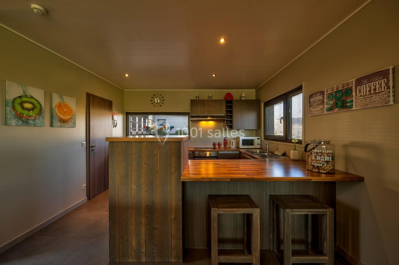 Cuisine moderne avec comptoir en bois, tabourets, électroménagers, décorations murales et éclairage chaleureux.