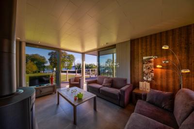 Terrasse en bois avec table et chaises, vue sur un jardin verdoyant et un lac au coucher du soleil.
