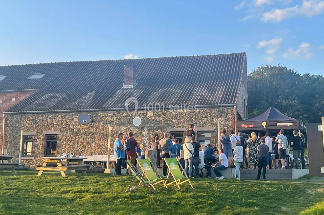 Groupe de personnes rassemblées devant un bâtiment en pierre avec des chaises longues sur une pelouse.