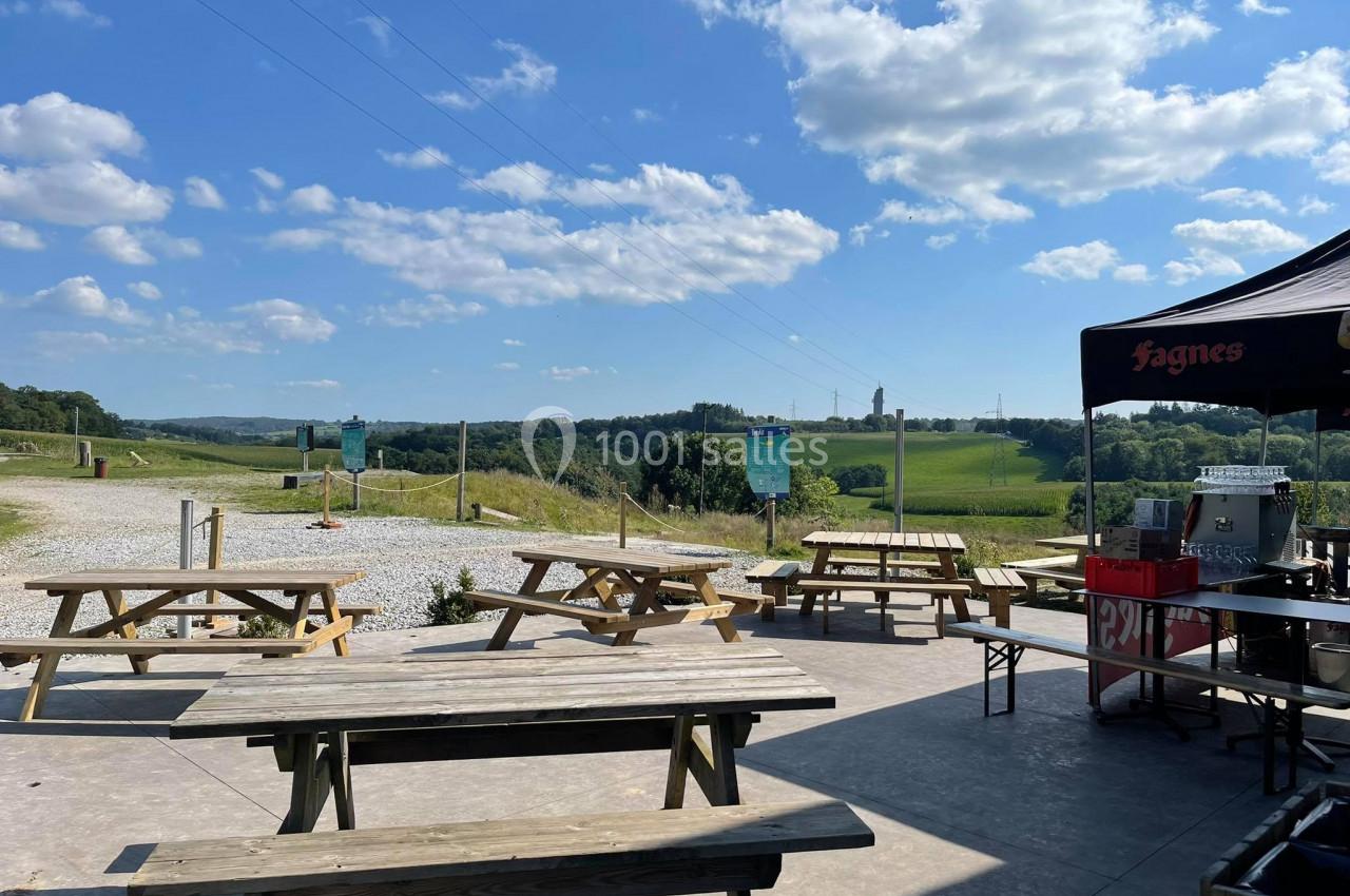 Tables de pique-nique en bois sur une terrasse avec vue sur une campagne vallonnée sous un ciel partiellement nuageux.