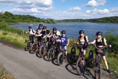 Dépliant sur des trottinettes électriques tout terrain posé sur une table avec viennoiseries et jus d'orange en arrière-plan.