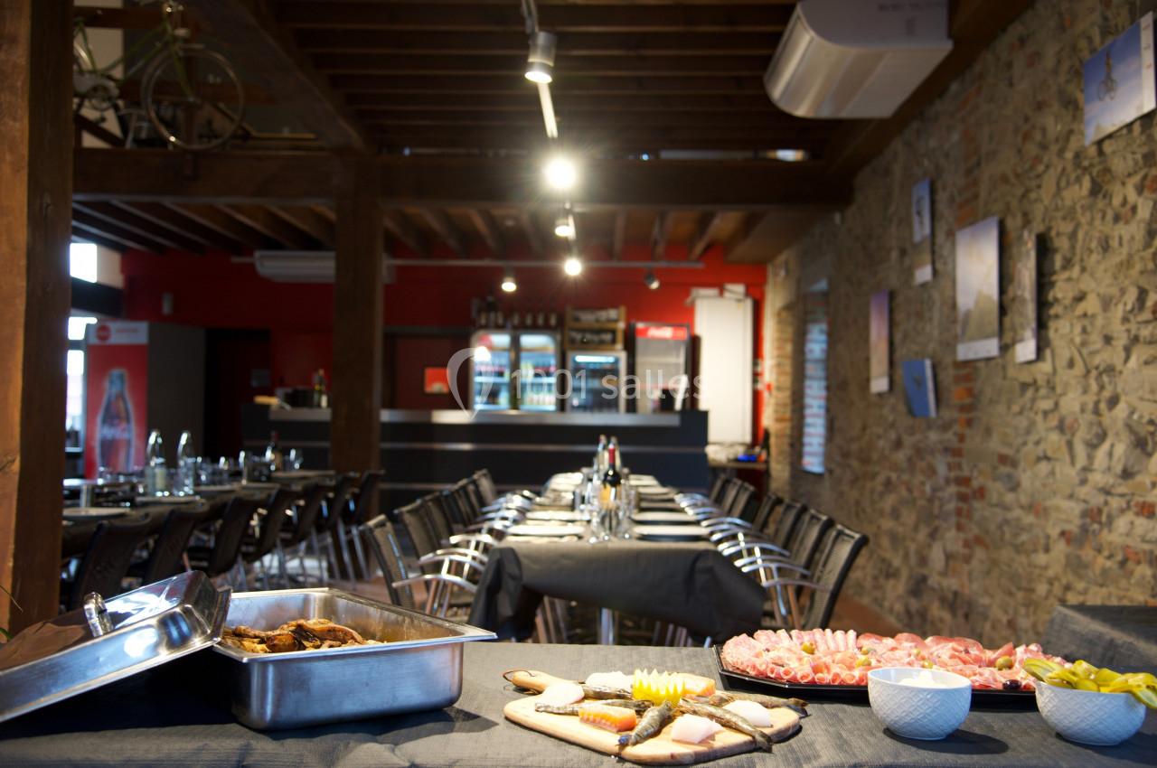 Salle de restaurant avec tables dressées, plats de charcuterie et buffet en premier plan, murs en pierre apparente.