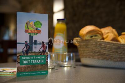 Dépliant sur des trottinettes électriques tout terrain posé sur une table avec viennoiseries et jus d'orange en arrière-plan.