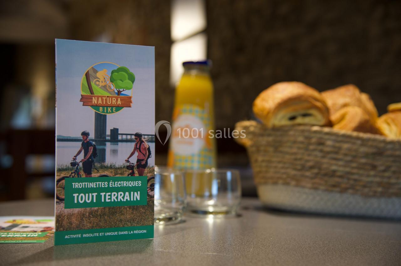 Dépliant sur des trottinettes électriques tout terrain posé sur une table avec viennoiseries et jus d'orange en arrière-plan.