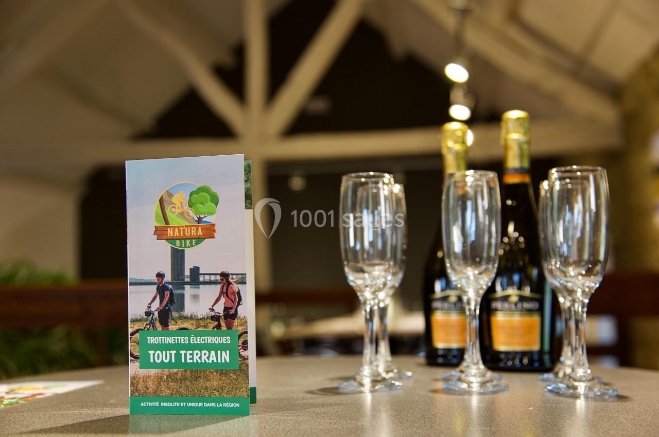 Dépliant sur une table avec des verres à pied et des bouteilles en arrière-plan dans un espace intérieur.
