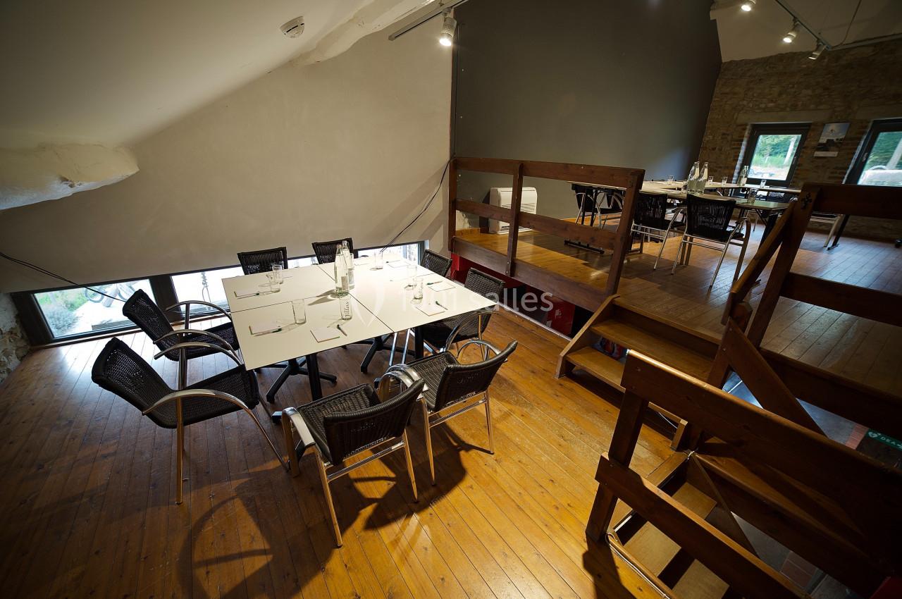 Salle à manger lumineuse avec parquet en bois, tables blanches, chaises noires et mezzanine en bois.