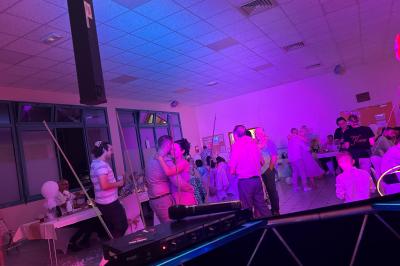 Des personnes dansent dans une salle éclairée par des lumières rouges, entourées de tables dressées pour un événement.